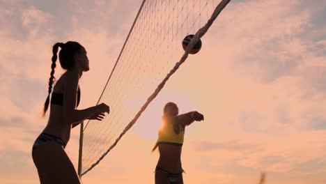 SLOW-MOTION-LOW-ANGLE-CLOSE-UP-SUN-FLARE:-Athletic-girl-playing-beach-volleyball-jumps-in-the-air-and-strikes-the-ball-over-the-net-on-a-beautiful-summer-evening.-Caucasian-woman-score-a-point.
